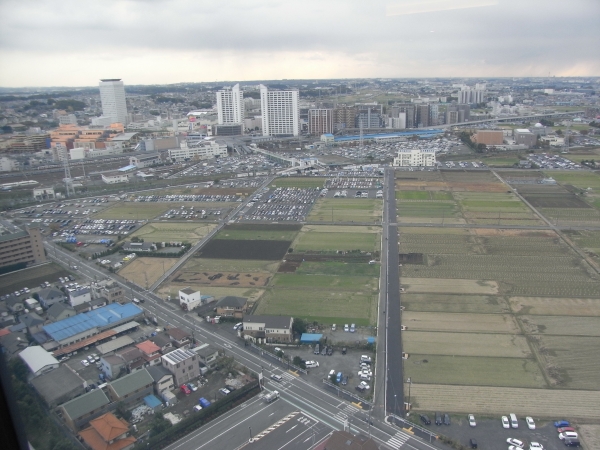 駅からの通路　あぜ道のような通りが舗装、拡張され、濃いグレーが歩道で左が車道　でもっと左の肌色が丸井