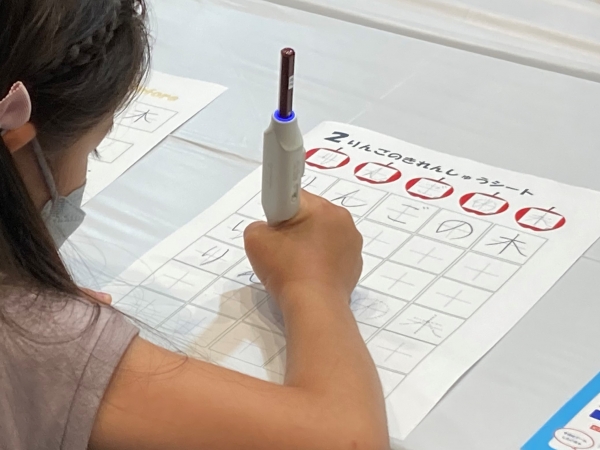 教わったとおりに美文字に挑戦する子ども達 しゅくだいやる気ペンのLEDの色の変化を楽しみながら、教わったとおりに「リンゴの木」を書く子どもの姿