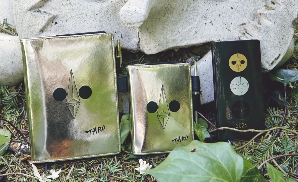 岡本太郎の代表作『太陽の塔』が手帳に。「黄金の顔」をデザインした手帳カバーと、正面の「太陽の顔」、背面の「黒い太陽」を加えた3つの顔を並べたweeksが登場